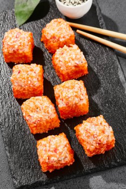 Kara tahtada fırında Maki suşisi. Yengeçli sıcak California maki. Masugo 'lu suşi rulosu, fırında peynir ve yengeç. Siyah arka planı, yaprakları ve sert gölgesi olan Japon tarzı bir menü.