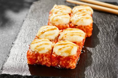 Kara tahtada fırında Maki suşisi. Peynirli sıcak California maki. Dışarıda tobiko soslu, fırında peynirli suşi rulosu. Siyah arka planı, yaprakları ve sert gölgesi olan Japon tarzı bir menü.