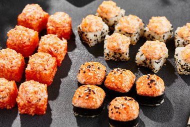 Ateşli maki, kara tahta üzerine kurulmuş. Fırında suşi ve sıcak ekmek. Somon, tobiko ve fırında peynirli suşi. Siyah arka planı, yaprakları ve sert gölgesi olan tarz konsept suşi menüsü