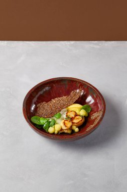 Kereviz ezmeli kızarmış deniz tarağı ve koyu el yapımı seramik tabakta kabak topları. Gri beton arka planda modern servis malzemeleriyle deniz ürünleri tabağı. İlham verici şef.