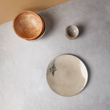 Gri taşlı arka planda modern tarzda seramik bulaşık takımı. Minimalist kompozisyonda boş el yapımı çanak çömlek. Beton arka planda çömlek plakası