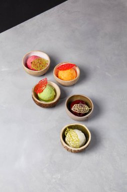 Seramik tabaklarda çeşitli dondurma topları. Donmuş tatlı - vanilyalı dondurma, fıstıklı, mangolu, yabanmersinli ve çilekli gri taşlı arka plan. Gelato 'dan minimal bileşim