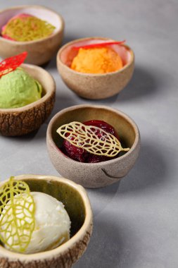 Seramik tabaklarda çeşitli dondurma topları. Donmuş tatlı - vanilyalı dondurma, fıstıklı, mangolu, yabanmersinli ve çilekli gri taşlı arka plan. Gelato 'dan minimal bileşim
