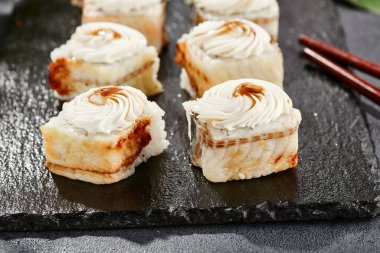 Kara tahtada Maki suşisi. Yılanbalıklı Unagi maki. Yılanbalığı, krem peynir ve unagi soslu suşi. Siyah arka planı, yaprakları ve sert gölgesi olan Japon tarzı bir menü.