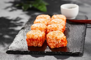 Kara tahtada fırında Maki suşisi. Sıcak California maki ve tobiko. Masaj havyarlı suşi rulosu, fırının üstünde peynir. Siyah arka planı, yaprakları ve sert gölgesi olan Japon tarzı bir menü.