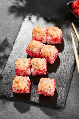 Kara tahtada fırında Maki suşisi. Somonlu sıcak suşi. Dışarıda tobiko ile suşi rulosu, fırında balık ve peynir. Siyah arka planı, yaprakları ve sert gölgesi olan Japon tarzı bir menü.