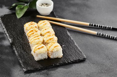 Kara tahtada fırında Maki suşisi. Unagi soslu sıcak peynirli maki. Üstünde fırında peynir ve unagi soslu suşi rulosu. Siyah arka planı, yaprakları ve sert gölgesi olan Japon tarzı bir menü.