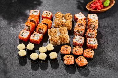 Maki suşisi koyu arkaplanda. Çeşitli ekmeklerle Maki seti. Suşi börekleri ve fırında maki karışımı. Siyah arka planı, yaprakları ve sert gölgesi olan tarz konsept suşi menüsü