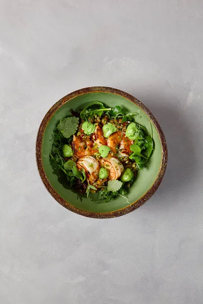 Yeşil kase, karides, kinoa ve el yapımı seramik tabakta avokado kreması. Karanlık modern bulaşık takımında karidesli salata. Modern tarzda sağlıklı yiyecekler..