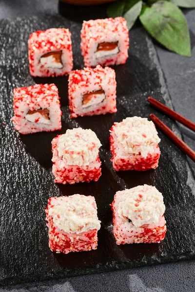 Kara tahtada Maki suşisi. Yengeçli Maki dürümü. Yengeç, krem peynir ve tobika ile suşi rulosu. Siyah arka planı, yaprakları ve sert gölgesi olan Japon tarzı bir menü.