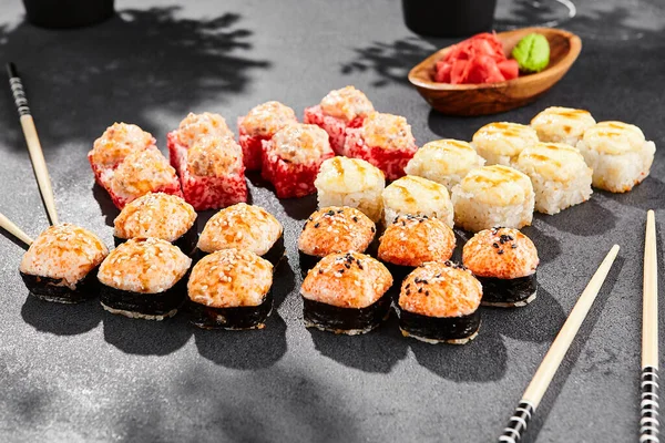Hot maki set on dark slate. Baked sushi set with variety rolls. Sushi rolls with salmon,tobiko, crab and baked cheese topped. Style concept sushi menu with black background, leaves and hard shadow