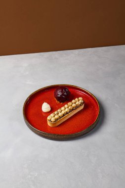 Kırmızı seramik bulaşık takımında böğürtlenli dondurmalı fındık tartı. Minimalist tarzda karamel ve fındıklı tart. Gri taş arka planda modern tatlı