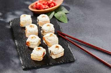 Kara tahtada Maki suşisi. Yılanbalıklı Unagi maki. Yılanbalığı, krem peynir ve unagi soslu suşi. Siyah arka planı, yaprakları ve sert gölgesi olan Japon tarzı bir menü.