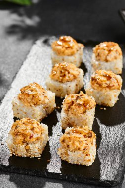 Kara tahtada fırında Maki suşisi. Yılanbalıklı sıcak unagi maki. Fırında yılan balığı, peynir ve unagi soslu suşi rulosu. Siyah arka planı, yaprakları ve sert gölgesi olan Japon tarzı bir menü.