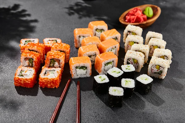 Maki sushi set on dark slate. Maki set with variety rolls. Composition from sushi rolls - philadelphia, california, hosomaki . Style concept sushi menu with black background, leaves and hard shadow