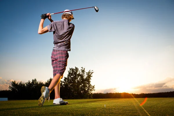 Hombre jugador de golf teeing off pelota de golf de tee box a hermosa puesta de sol —  Fotos de Stock