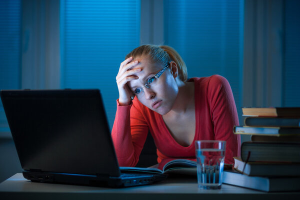 Young bored female college student studying poorly at late evening