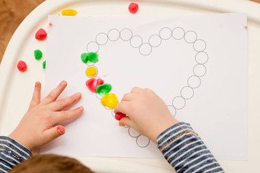 Annem için sevgililer günü tebrik kartı hazırlıyorum. Küçük çocuk baskılı kağıt kalbe hamur uyguluyor. Güzel motor beceriler, parmak koordinasyonu. bebekler için erken eğitim