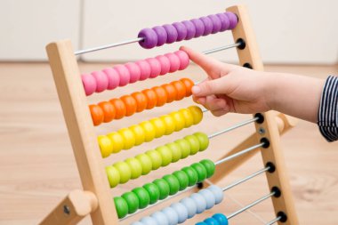 A cute kid is playing with an abacus at home. A smart child learns to count. Wooden figure necklace. A tool for children to develop fine motor skills, logical thinking.