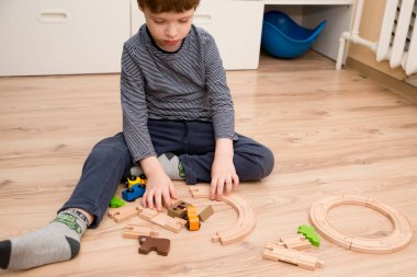 Boy plays with wooden toys. Railway and train with animal wagons on wooden floor. Nostalgia toy from childhood.