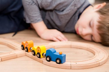 Boy plays with wooden toys. Railway and train with animal wagons on wooden floor. Nostalgia toy from childhood.