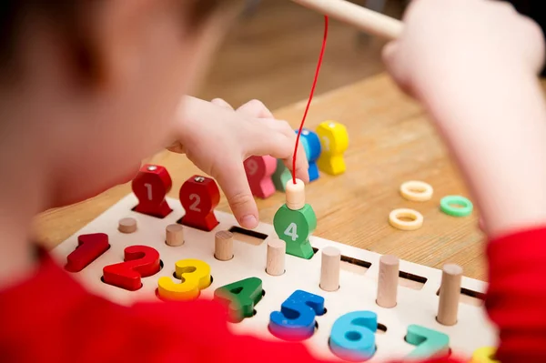 Çocuk farklı renkte ahşap halkalarla oynuyor. Sıralama, iyi motor beceriler, eğitim ve beyin egzersizi için terapi görevi. Matematik oyunu da dahil. Montessori tipi uygulama. Tahta oyuncaklar.