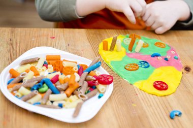 Paskalya konsepti. Çocuk renkli erişteleri yumurta şeklindeki plastiğin üzerine yerleştiriyor. Çocuklar ev fikirleri için oyuncak, çocuk istihdam, iyi motor beceriler, ergoterapi, duyusal terapi