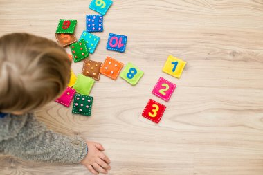 Yürüyen çocuk yerde oynuyor. Ev yapımı oyun: Doğru çifti bul. Farklı renkte doldurulmuş kare şeklinde sayılar ve eş domino benzeri noktalar. Erken eğitim, öğrenme rakamları.