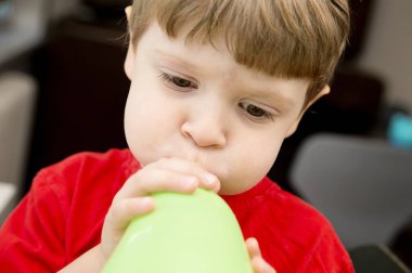 Ağızlı yeşil balon şişiren 3 yaşında bir çocuk. Şişmiş yanaklar ve şişmiş gözler. Akciğerler, nefes egzersizi. Soluk aksesuarlar.