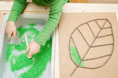 Çocuk yeşil renkli pirinçle oynuyor. Çocukların oyun yoluyla iyi motor becerileri geliştirmesi için uygulama. El-göz koordinasyonunu öğrenmek için DIY oyuncağı.