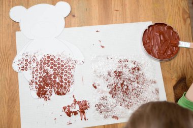 Ev yapımı balonlu film boyama tekniği ve göbeğine ponpon topları yapıştırılmış oyuncak ayı. Küçük çocuk üretim aşamasında..