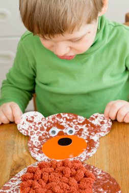 Ev yapımı balonlu film boyama tekniği ve göbeğine ponpon topları yapıştırılmış oyuncak ayı. Küçük çocuk üretim aşamasında..