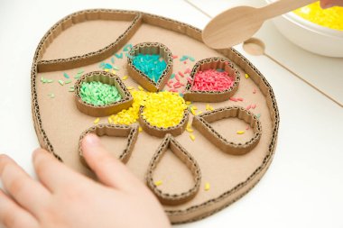 Paskalya yumurtasını renkli pirinçle süslemek. Çocukların oynarken motor becerilerini geliştirmeleri için bir araç. El-göz koordinasyonu için DIY oyuncağı.