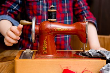 Meslek öğreniyorum. Çocuk mekanik el dikiş makinesiyle elbise dikiyor. Retro oyuncak, orijinalinin indirimli kopyası. Evdeki etkinlikler. Gerçek profesyonelin sanatsal taklidi..