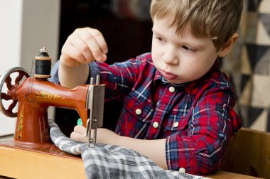 Meslek öğreniyorum. Çocuk mekanik el dikiş makinesiyle elbise dikiyor. Retro oyuncak, orijinalinin indirimli kopyası. Evdeki etkinlikler. Gerçek profesyonelin sanatsal taklidi..