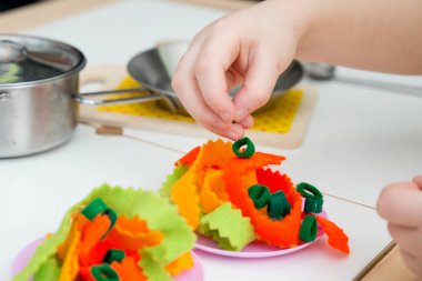 Anne, yemek zamanı! Çocuk oyuncak mutfağında oyuncak yemek hazırlıyor. Çocuk yetişkin sorumluluklarını taklit ediyor. Evdeki etkinlikler. Yaratıcılığı teşvik eden bir oyun. Makarna hissettim..