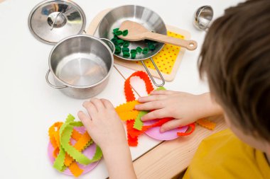 Anne, yemek zamanı! Çocuk oyuncak mutfağında oyuncak yemek hazırlıyor. Çocuk yetişkin sorumluluklarını taklit ediyor. Evdeki etkinlikler. Yaratıcılığı teşvik eden bir oyun. Makarna hissettim..