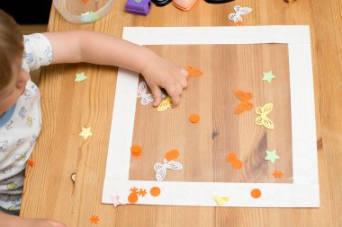 Çocuk cam süslemesi yapıyor. Çerçevelenmiş yapışkan filme kağıt kelebekler takıyor. Dolayısıyla rahatlama ve eğlence amaçlı terapi görevi. Çocuklar ve engelliler için iyi motor becerileri.