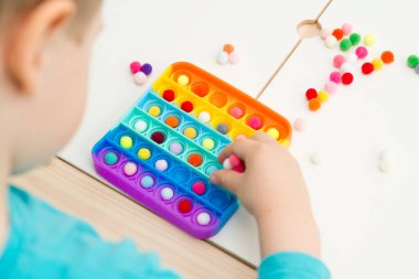Çocuk duyusal oyuncak Pop-it ile oynuyor. Kaliteli motor becerileri için araç, saymaya başlamak için araç, birincil aritmetik işlemlerini öğrenmek. Parmak uyumu ve rahatlama için bir yatıştırıcı..
