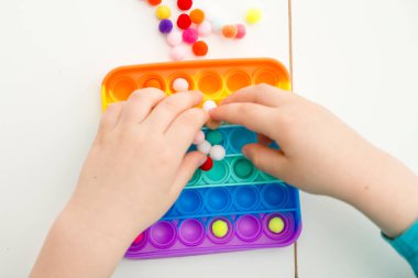 Çocuk duyusal oyuncak Pop-it ile oynuyor. Kaliteli motor becerileri için araç, saymaya başlamak için araç, birincil aritmetik işlemlerini öğrenmek. Parmak uyumu ve rahatlama için bir yatıştırıcı..