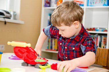 Oyun hamuruyla yemek pişirmek. Çocuk farklı renkte plastiklerle ve plastik mutfak malzemeleriyle oynuyor. Küçük çocuğun sanatsal yüz ifadesi.