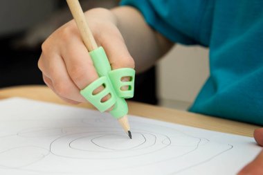 Kalem tutacağıyla yazan çocuk. Silikon yardım tutuşu kalemi doğru pozisyonda tutmak için öğrenmeye ve pratik yapmaya yardımcı olur. El yazısının düzeltilmesi veya rehabilitasyonu.