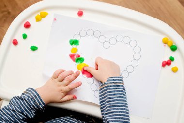 Annem için sevgililer günü tebrik kartı hazırlıyorum. Küçük çocuk baskılı kağıt kalbe hamur uyguluyor. Güzel motor beceriler, parmak koordinasyonu. bebekler için erken eğitim