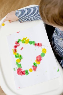 Annem için sevgililer günü tebrik kartı hazırlıyorum. Küçük çocuk baskılı kağıt kalbe hamur uyguluyor. Güzel motor beceriler, parmak koordinasyonu. bebekler için erken eğitim