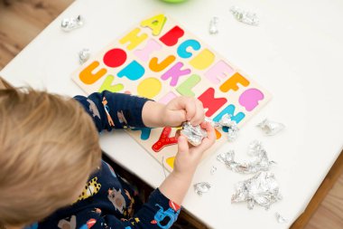Tahta alfabe harfleriyle oynayan iki yaşında bir çocuk. Folyoya sarılı mektuplar. Entellektüel oyun, erken eğitim için anaokulu uygulaması. Sözlü ve bellek alıştırması.