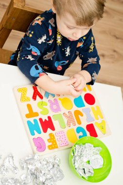 Tahta alfabe harfleriyle oynayan iki yaşında bir çocuk. Folyoya sarılı mektuplar. Entellektüel oyun, erken eğitim için anaokulu uygulaması. Sözlü ve bellek alıştırması.