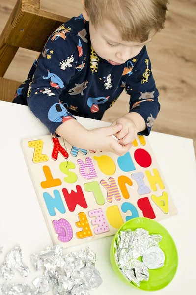 Tahta alfabe harfleriyle oynayan iki yaşında bir çocuk. Folyoya sarılı mektuplar. Entellektüel oyun, erken eğitim için anaokulu uygulaması. Sözlü ve bellek alıştırması.