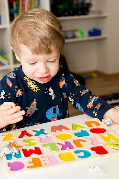Tahta alfabe harfleriyle oynayan iki yaşında bir çocuk. Folyoya sarılı mektuplar. Entellektüel oyun, erken eğitim için anaokulu uygulaması. Sözlü ve bellek alıştırması.