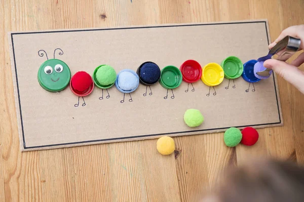 Plastik şişe kapağı solucanı. Doğru renk ponponları kırkayak tırtılına koyun. Beş dakikalık el işi. Çocuk yuvası aktivitesi. Erken eğitim, iyi motor becerileri. # Evde kal.