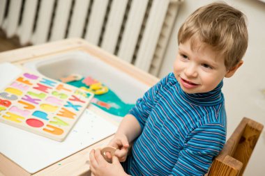 Çocuk oyun boyunca alfabe okumayı öğreniyor. Renkli pirinç ve ahşap harflerle duyusal aktivite. Evde eğitim, okul öncesi eğitim, Montessori metodu